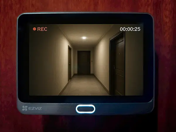 La mirilla Ezviz CP4 grabando un vídeo de un pasillo de un edificio. La imagen en la pantalla es clara y abarca todo el pasillo, incluyendo varias puertas, lo que demuestra la calidad de su cámara y su cobertura de gran angular.