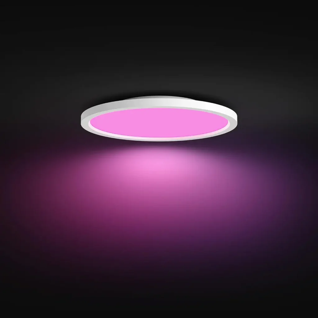 Plafón LED inteligente Philips Hue Devote de color blanco, instalado en un techo oscuro y emitiendo una luz ambiental de color rosa intenso para crear una escena de iluminación personalizada.