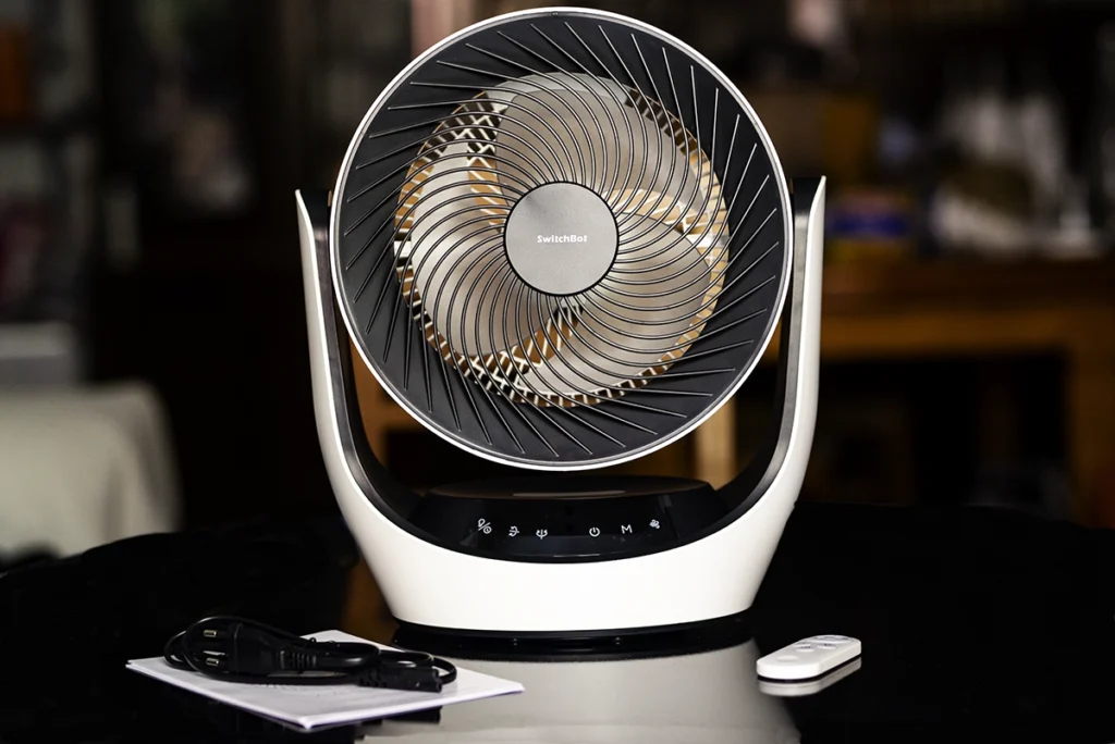 Ventilador de mesa inteligente SwitchBot Battery Circulator Fan en color blanco y negro, mostrando su diseño con parrilla en espiral, los controles táctiles en la base, el mando a distancia y el cable de alimentación.
