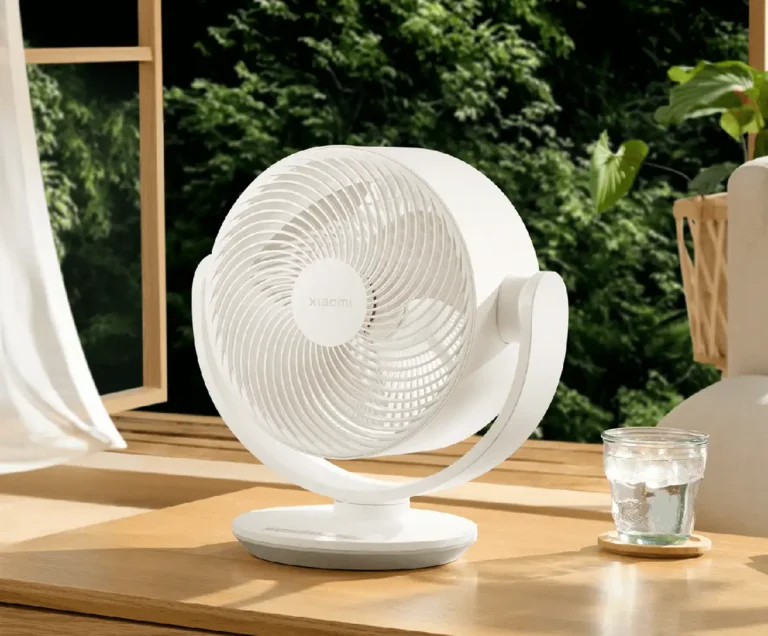 Primer plano del ventilador Xiaomi Smart Desktop Air Circulation Fan sobre una mesa de madera, junto a una ventana abierta, mostrando su diseño compacto y silencioso para refrescar el hogar.