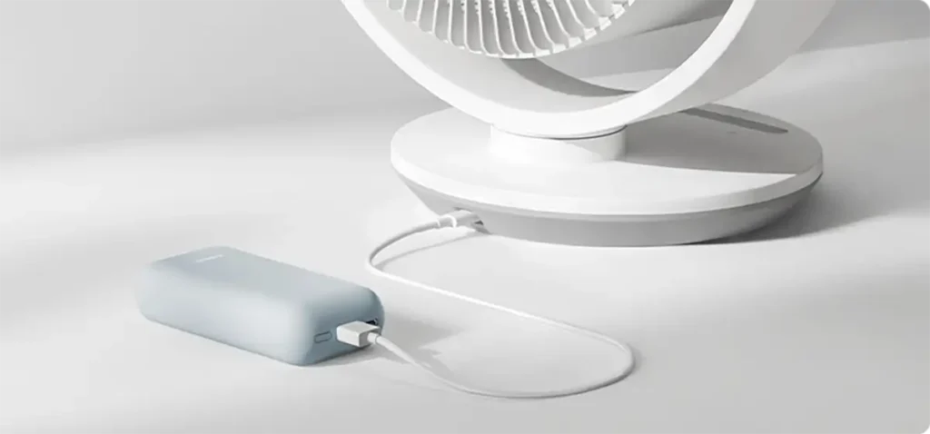 El ventilador Xiaomi Smart Desktop Air Circulation Fan conectado a una batería externa (power bank) a través de su puerto USB-C, demostrando su portabilidad.