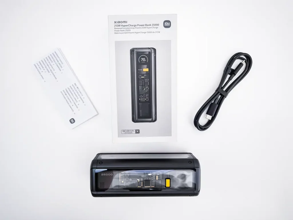 Unboxing de la Xiaomi 212W HyperCharge Power Bank sobre un fondo blanco. Se muestra la batería portátil con su diseño transparente, la caja del producto, un cable USB-C a USB-C negro y el manual de instrucciones