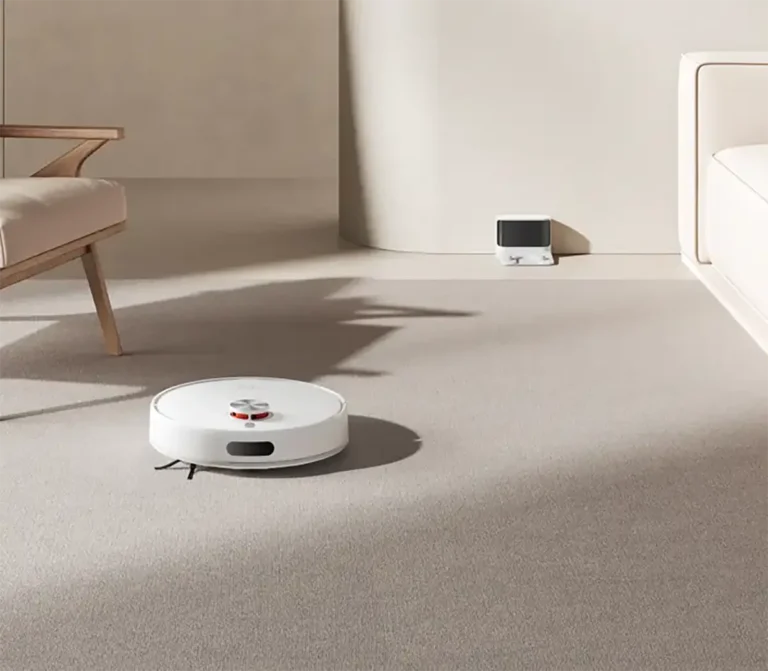 robot aspirador s40 blanco de Xiaomi sobre una alfombra gris en un salón de estilo minimalista. Al fondo se ve su base de carga junto a la pared