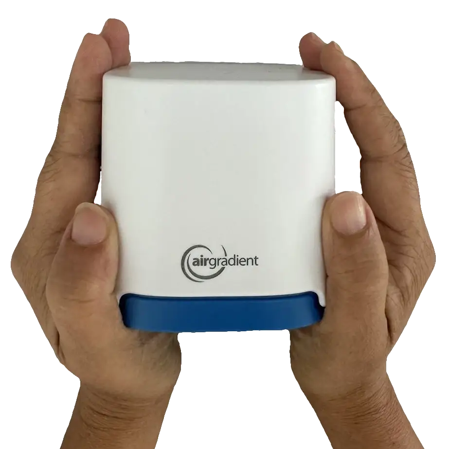 Manos sosteniendo el monitor de calidad del aire para exteriores AirGradient Open Air. Un dispositivo compacto y resistente, compatible con Home Assistant, diseñado para medir la polución y partículas en el exterior