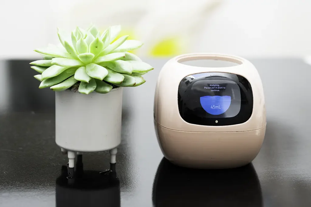 Proceso de configuración del macetero inteligente Ivy Smart Planter. La imagen muestra la pantalla del dispositivo en modo análisis, midiendo el nivel de agua (45mL) antes de insertar la maceta interior con la suculenta.
