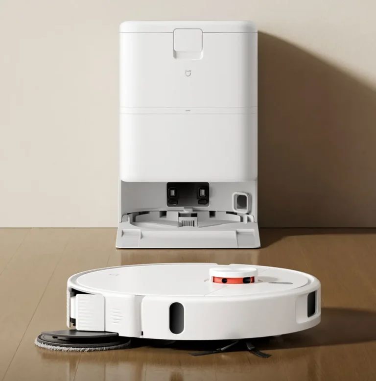 Robot aspirador Xiaomi Mijia Robot Vacuum & Mop 5C en blanco, mostrando su mopa extensible para la limpieza de bordes. Al fondo, su base de autolimpieza y autovaciado sobre un suelo de madera.