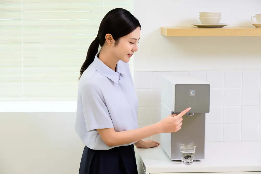 Mujer usando el panel de control táctil del purificador de agua Samsung Bespoke AI Water Purifier Countertop para servirse un vaso de agua en la encimera de su cocina.