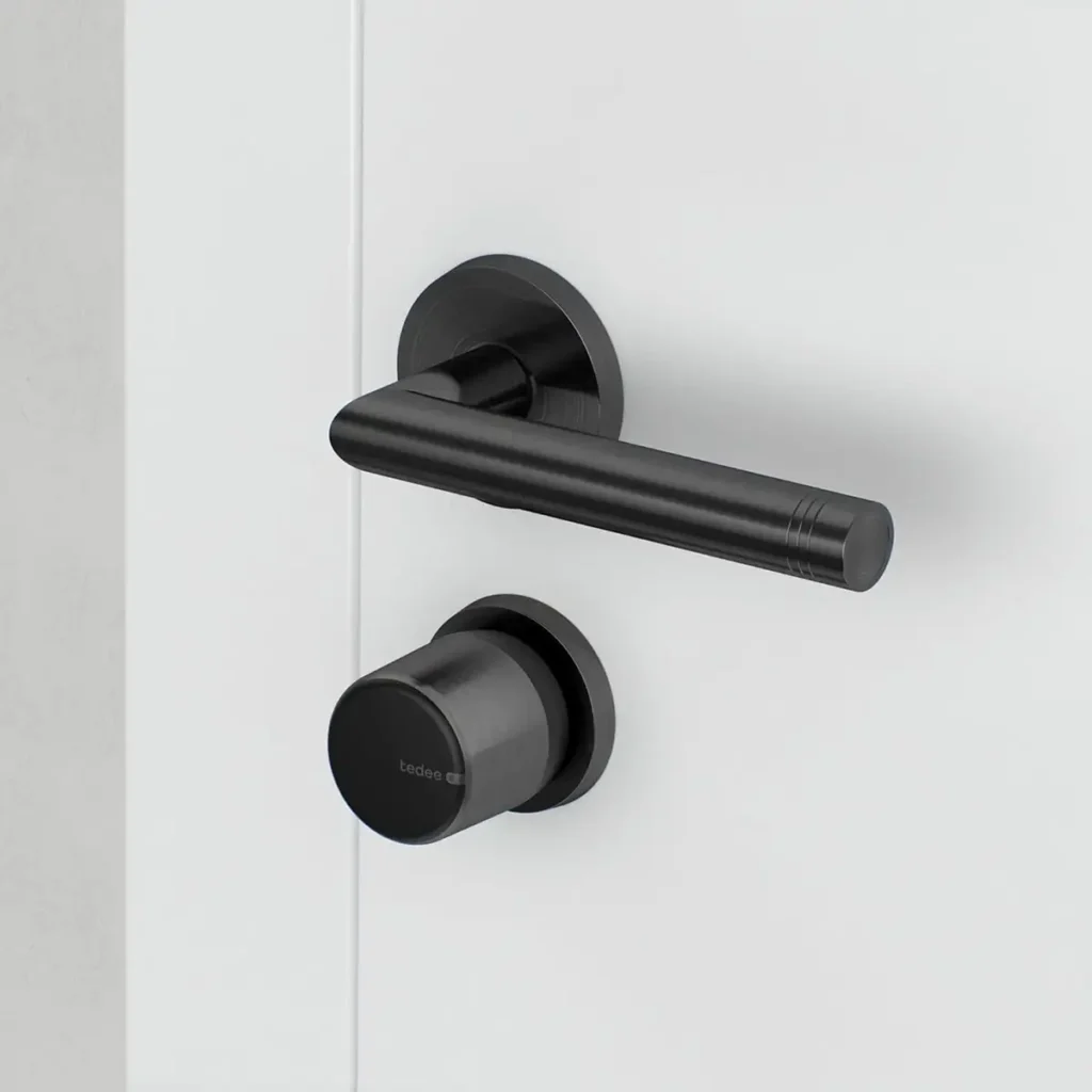 Cerradura inteligente Tedee GO2 de aluminio en color negro, instalada en el interior de una puerta blanca junto a una manilla a juego.