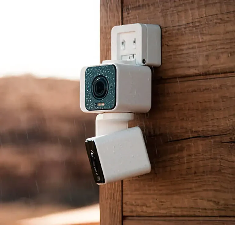 Texto ALT: Cámara de seguridad para exteriores Wyze Duo Cam Pan instalada en un poste de madera bajo la lluvia, demostrando su resistencia a la intemperie con certificación IP65.