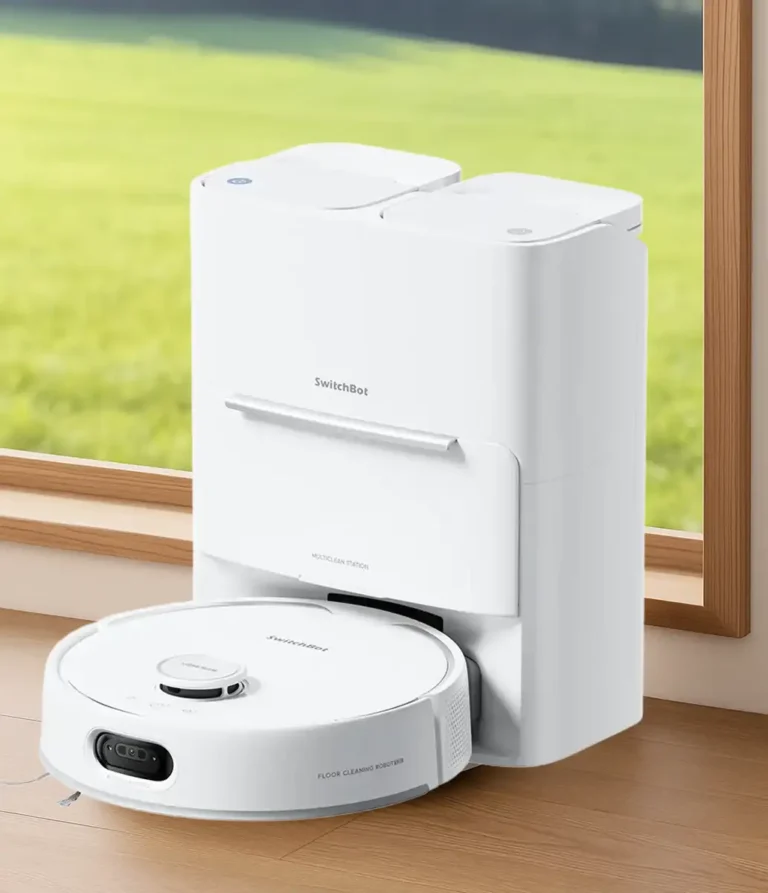 Foto de producto del robot aspirador y fregasuelos SwitchBot S20 acoplado a su estación de limpieza automática con depósitos de agua. El sistema completo se muestra en un hogar, sobre un suelo de madera y junto a una ventana con un fondo verde y luminoso.