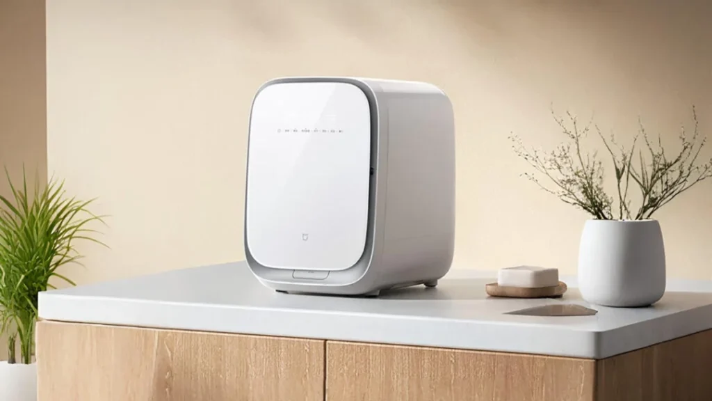 Lavadora-secadora compacta Xiaomi Mijia Mini Wash de color blanco, situada sobre una encimera blanca y un mueble de madera en un ambiente de hogar minimalista, ideal para el ahorro de espacio.