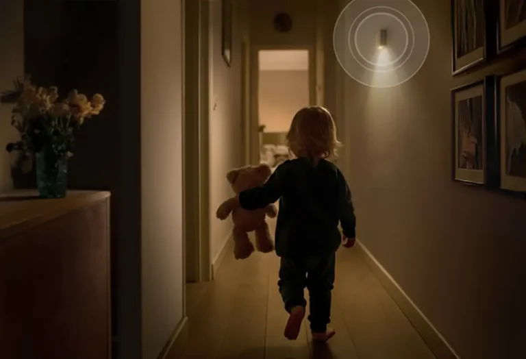 El Detector de Movimiento Bosch II [+M] iluminando un pasillo oscuro con su luz de orientación integrada mientras un niño camina de forma segura. La imagen ilustra la función de seguridad y confort del sensor compatible con Matter.