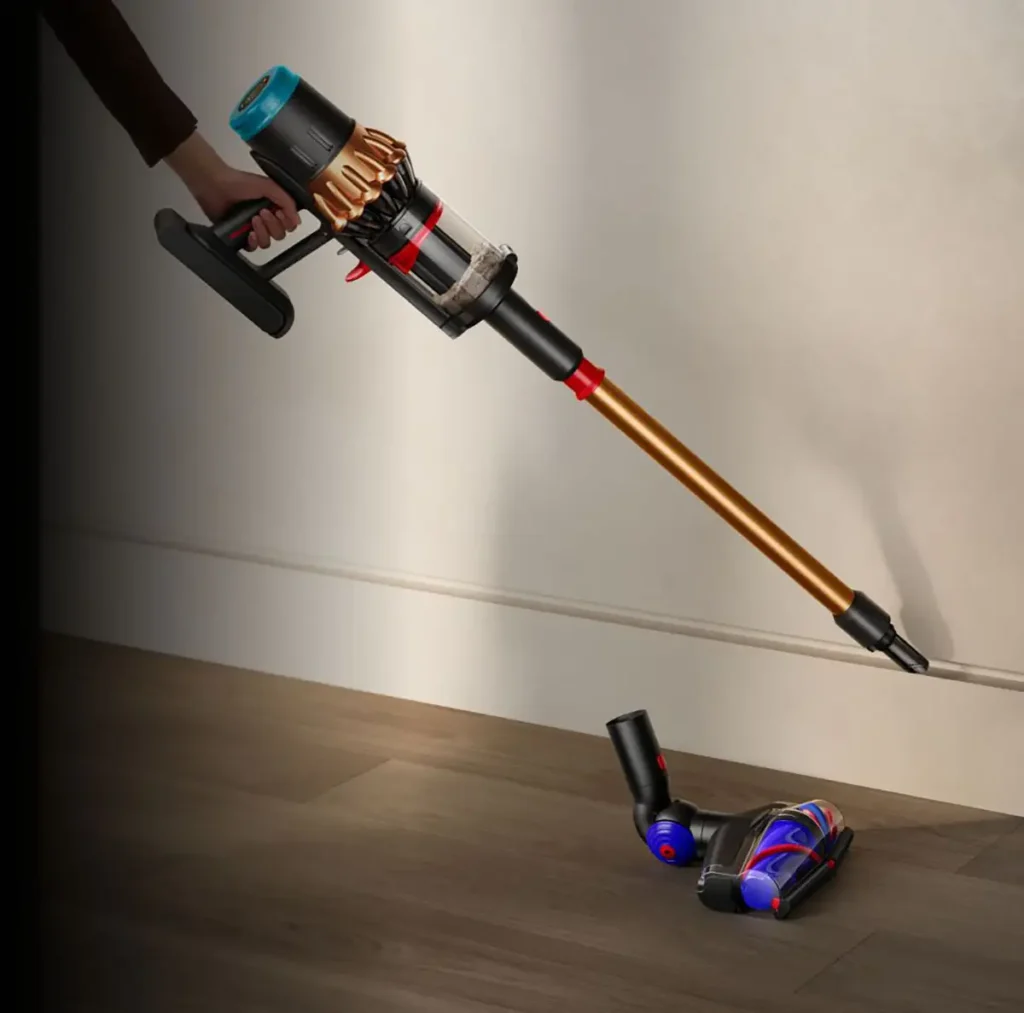 Imagen de la potente aspiradora sin cable Dyson V16 Piston Animal Submarine en un hogar moderno. Una persona utiliza el accesorio para rincones para una limpieza de precisión junto a un zócalo blanco, mientras que en el suelo de madera se muestra el cabezal principal, destacando su versatilidad para la limpieza completa de suelos duros.