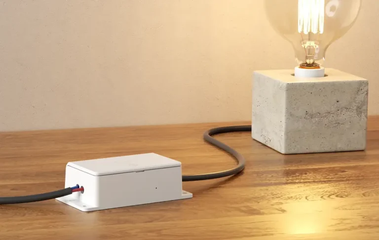 Interruptor inteligente Sonoff Basic Gen5 con Matter conectado en el cable de una lámpara de diseño sobre una mesa de madera, mostrando su uso como dispositivo en línea para domótica DIY