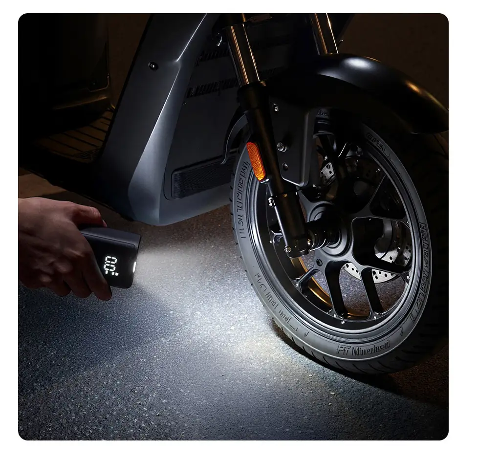 El inflador portátil Xiaomi Mijia Portable Inflator Mini utilizando su linterna LED integrada para iluminar el neumático de una motocicleta durante la noche. Esta función de seguridad, que también incluye un modo SOS, facilita el inflado de emergencia en condiciones de poca luz