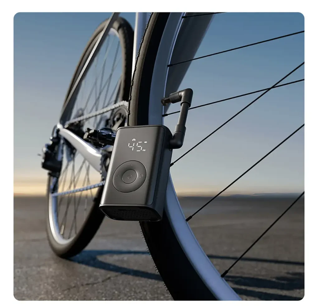 El inflador portátil Xiaomi Mijia Portable Inflator Mini conectado a la válvula de una rueda de bicicleta. La pantalla LCD muestra 45 PSI en el modo de inflado inteligente para ciclistas, demostrando su uso práctico y portabilidad para el mantenimiento de neumáticos.