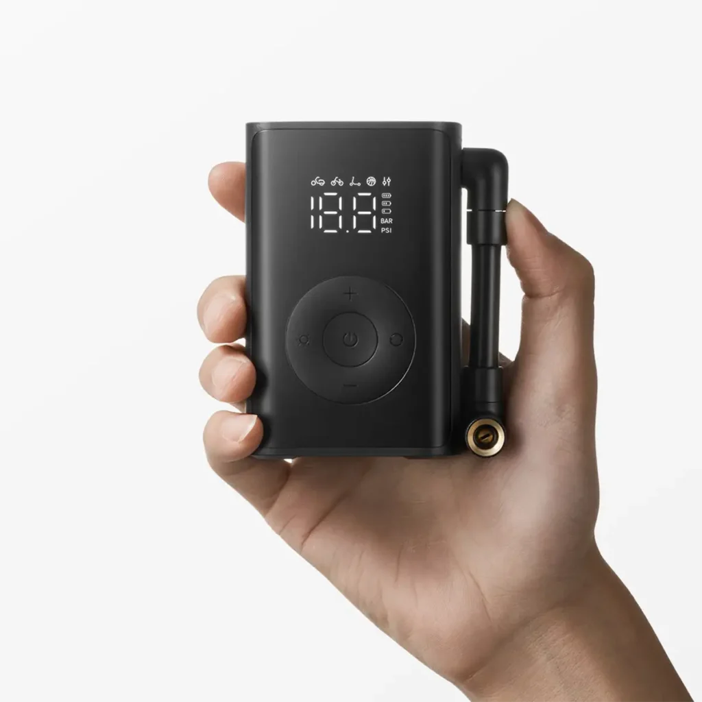 El inflador ultracompacto Xiaomi Mijia Portable Inflator Mini sostenido en la mano para mostrar su tamaño reducido y portabilidad. La pantalla LCD muestra los iconos de sus 5 modos de inflado inteligentes (bicicleta, moto, coche, etc.) y los controles de presión, destacando su diseño de bolsillo.