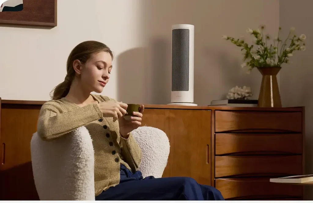 El calefactor inteligente Xiaomi Smart Graphene Heater mantiene un ambiente cálido y confortable, permitiendo a una mujer relajarse en su sillón con una bebida caliente.