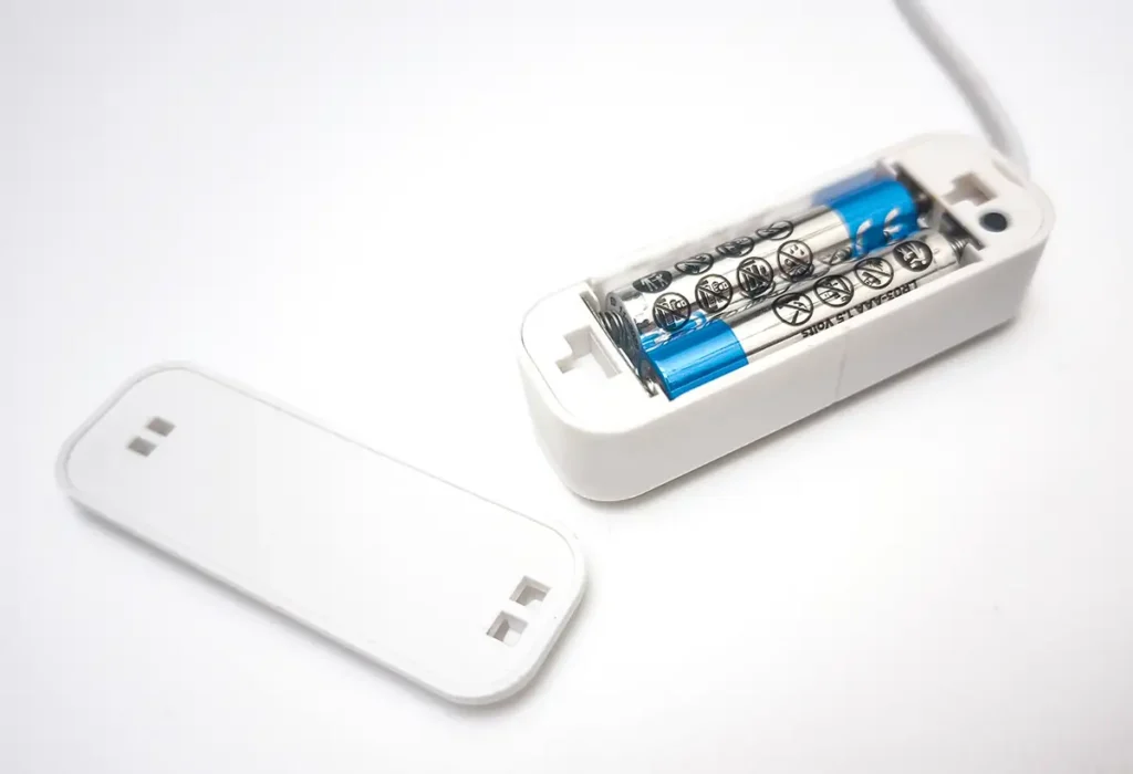 Interior del sensor de agua Tuya ONENUO 898GT, mostrando el compartimento de las dos pilas AAA (LR03) que lo alimentan. La tapa del dispositivo está retirada, revelando la simple construcción interna del sensor de fugas para domótica.