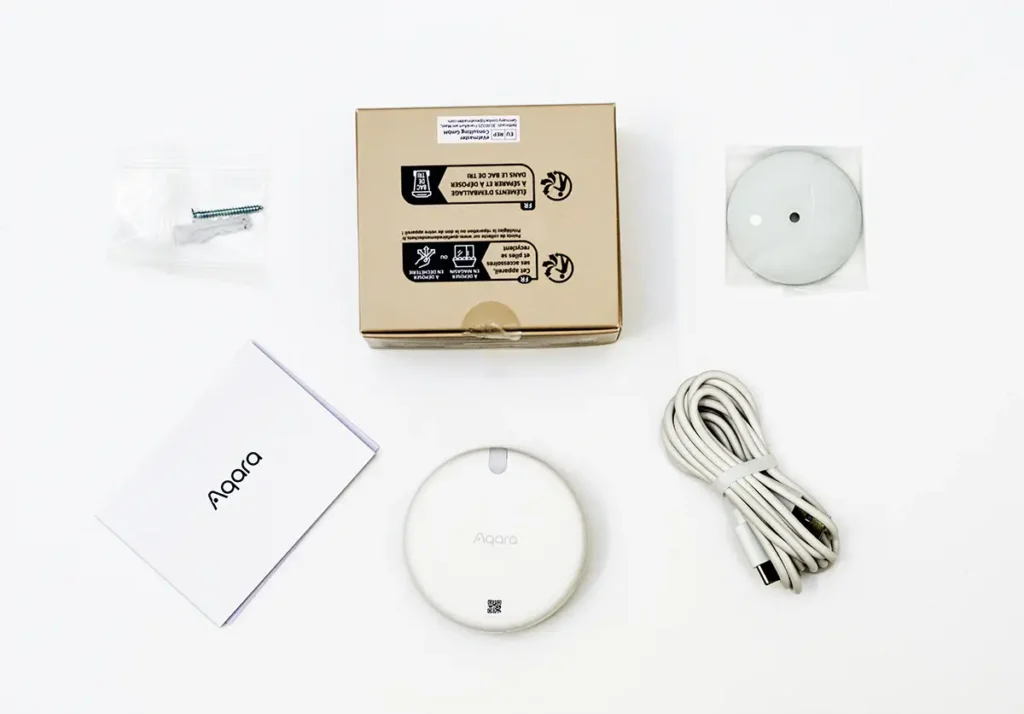 Unboxing del sensor de presencia Aqara FP2, mostrando el contenido completo de la caja: el sensor mmWave, el cable USB-C, la base de montaje magnética, el manual de usuario y los tornillos de instalación