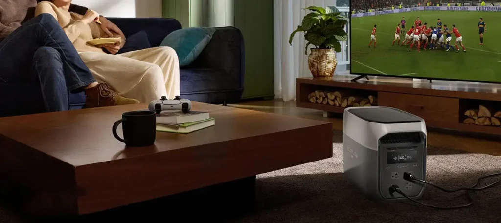 Estación de energía EcoFlow DELTA 3 Max alimentando un televisor en el salón mientras una pareja ve un partido de rugby, demostrando su uso como SAI/UPS para entretenimiento sin interrupciones durante un apagón.
