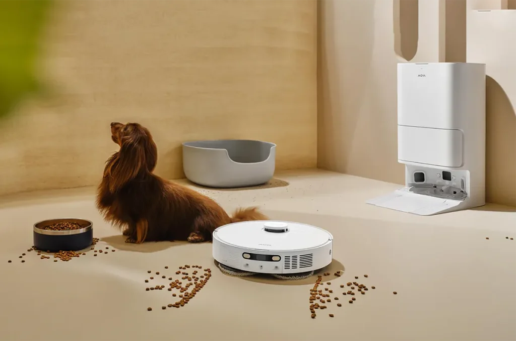 Robot aspirador Mova E40 Ultra demostrando su eficacia en hogares con mascotas al limpiar pienso de perro derramado del suelo. Al lado, un perro salchicha observa, destacando la función Clean Genius para áreas de mascotas y el cepillo antienredos.