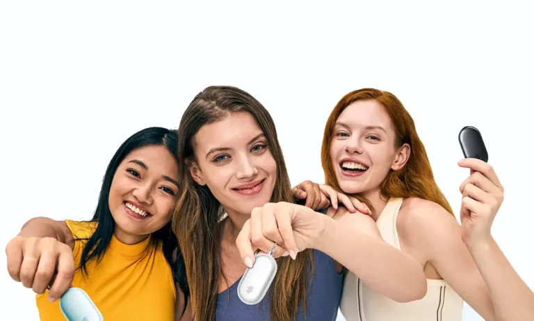 Imagen de portada promocional de la SwitchBot Safety Alarm. Tres mujeres jóvenes y felices miran a la cámara: una mujer a la izquierda con camiseta amarilla sostiene la versión aqua, la mujer del centro muestra la versión blanca, y la mujer de la derecha con pelo rojo sostiene la versión negra del dispositivo de seguridad.