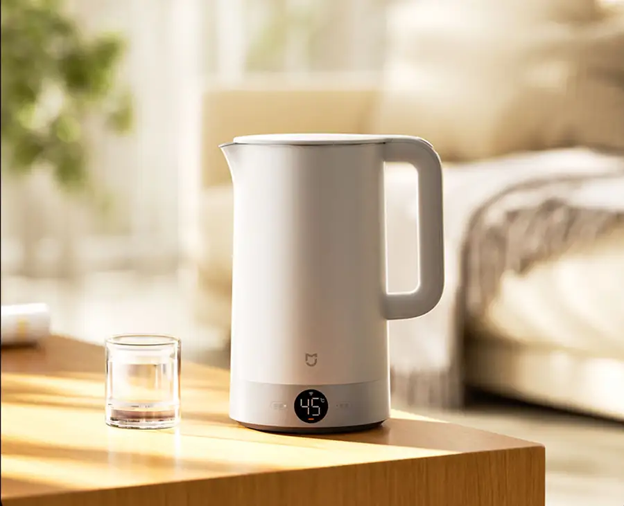Hervidor de agua inteligente Xiaomi Mijia Kettle 3 Pro sobre una mesa de madera en un ambiente de hogar moderno. El hervidor es blanco, su pantalla digital marca 45°C y muestra su función para mantener el agua a la temperatura ideal para bebidas.