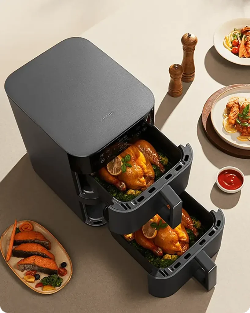 Vista superior de la freidora de aire Xiaomi Dual Zone Air Fryer 10L con sus dos cestas extraídas, mostrando dos pollos enteros asándose sobre una cama de brócoli. La imagen demuestra la capacidad de cocinar dos platos principales al mismo tiempo.