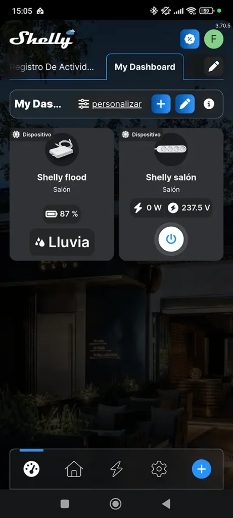 Dashboard principal de la app Shelly Cloud mostrando el widget del sensor Shelly Flood. La tarjeta del dispositivo indica un 87% de nivel de batería y muestra una alerta activa de "Lluvia", confirmando la detección de agua en tiempo real.
