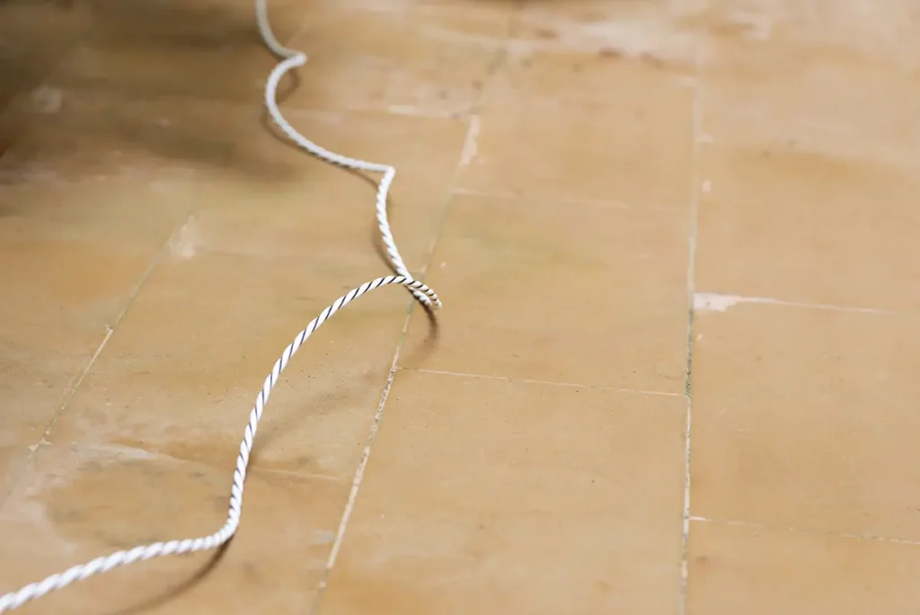 Detalle del cable detector del sensor Shelly Flood Gen4 extendido sobre un suelo de baldosas. La imagen ilustra la rigidez del cable, un aspecto clave a considerar al planificar el recorrido para cubrir el perímetro de una fuga.
