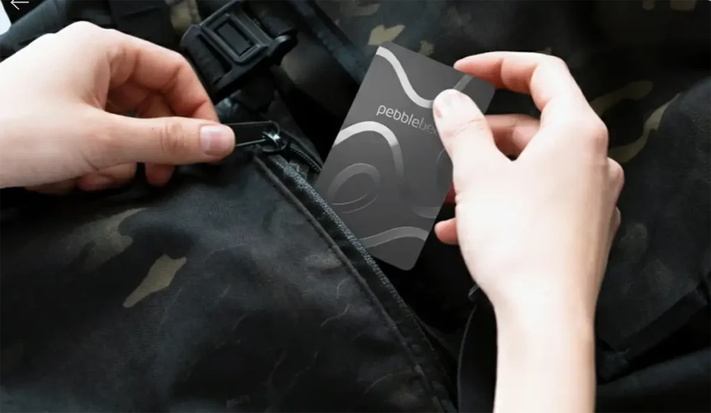 Una persona guardando la tarjeta localizadora ultrafina Pebblebee Card 5 en el bolsillo con cremallera de una mochila.