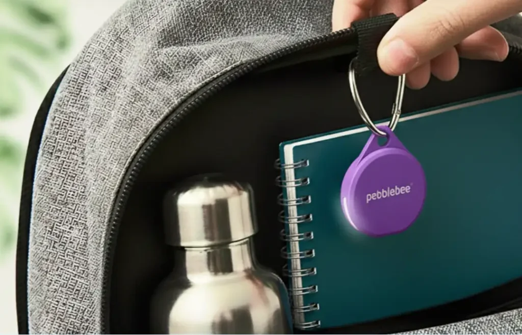 Localizador Bluetooth Pebblebee Clip 5 de color morado con su luz LED encendida, colgado del interior de una mochila gris.