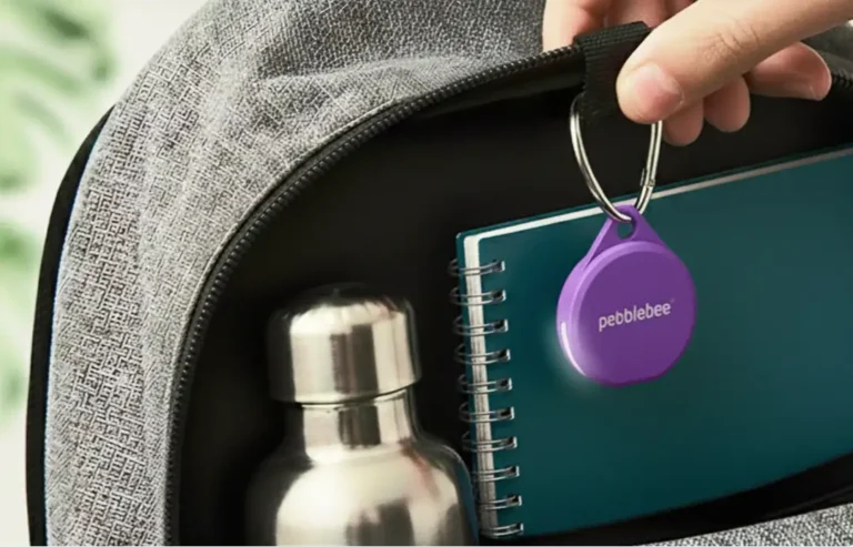 Localizador Bluetooth Pebblebee Clip 5 de color morado con su luz LED encendida, colgado del interior de una mochila gris.