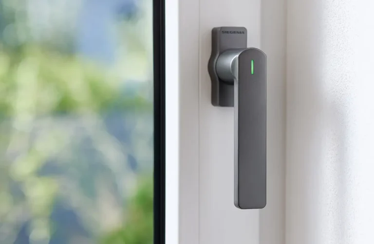 Manilla de ventana inteligente SIEGENIA Smart Window Handle Gen. 2 en color antracita, instalada en una ventana blanca de PVC. El LED de estado está iluminado en verde, indicando que está activa.