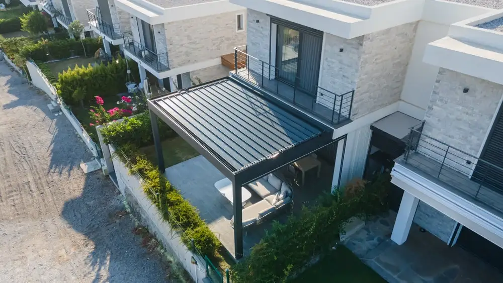 Vista aérea de una vivienda moderna con pérgola bioclimática en la terraza, protegida por lamas motorizadas y rodeada de jardín, ideal para automatizar según el tiempo.