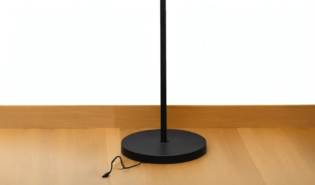 Base circular metálica negra de la lámpara de pie Govee Torchiere sobre suelo de madera, con el cable de alimentación saliendo por la parte inferior.
