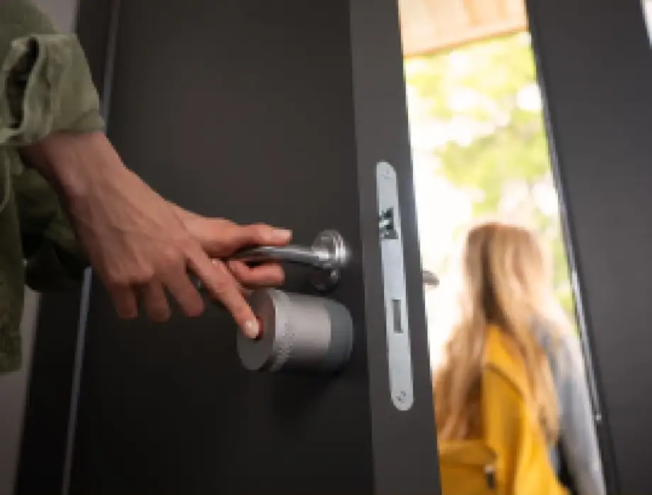 Persona cerrando una puerta desde el interior mientras pulsa la cerradura inteligente Yale Linus L2 Lite instalada sobre el cilindro