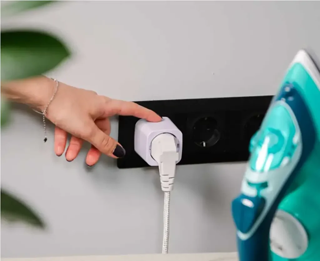 Shelly Plug M Gen3 blanco conectado a una toma de corriente junto a una plancha