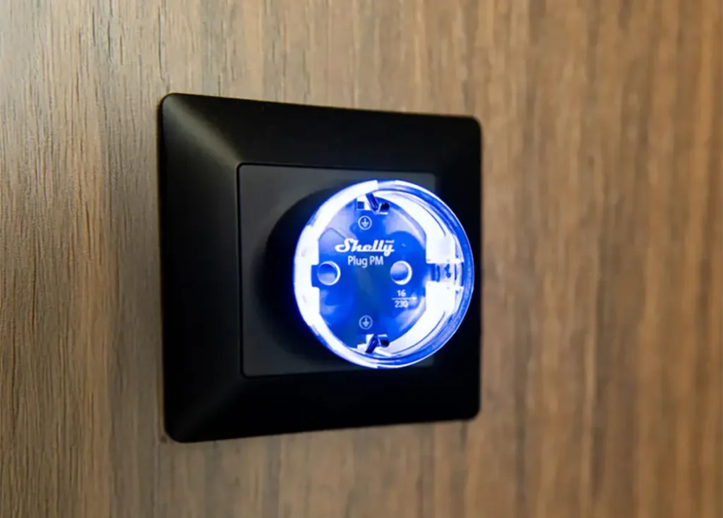 Shelly Plug PM Gen3 con anillo LED azul instalado en una toma de pared