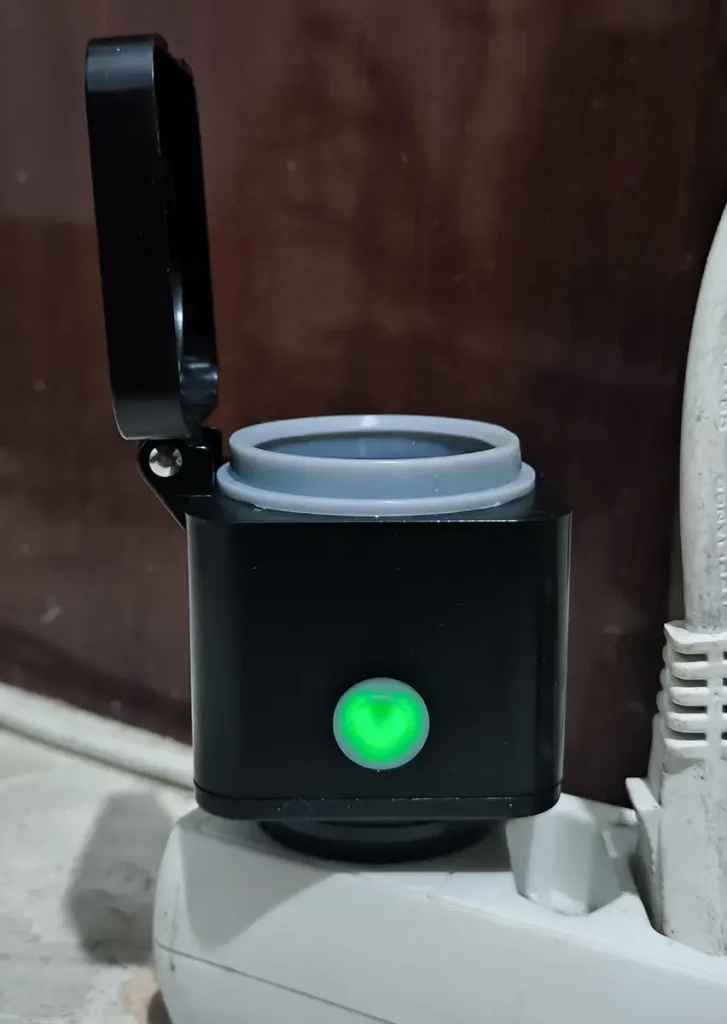 Luz LED verde del enchufe exterior Innr OSP 240 encendido, con la tapa abatible abierta y el dispositivo conectado en una regleta.