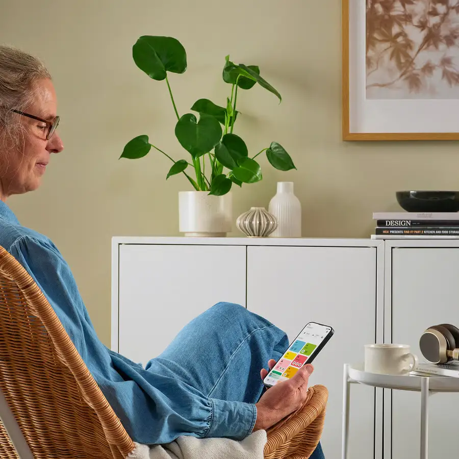 Persona usando la app IKEA Home smart para controlar dispositivos del hogar inteligente desde el móvil en el salón.