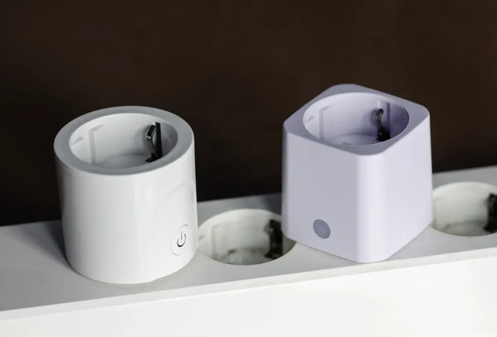 SwitchBot Plug Mini y Shelly Plug M Gen3 colocados en una regleta, mostrando la diferencia entre el diseño redondo del modelo de SwitchBot y el formato cuadrado del Shelly.