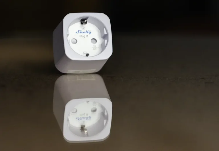 Shelly Plug M Gen3 sobre una superficie reflectante, mostrando el diseño cuadrado del enchufe inteligente con Matter y medición de consumo.