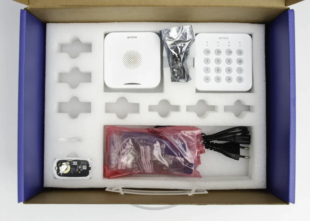 Segunda capa del kit de alarma ANNKE con sirena interior, teclado numérico, mando, accesorios de montaje y cable de alimentación.