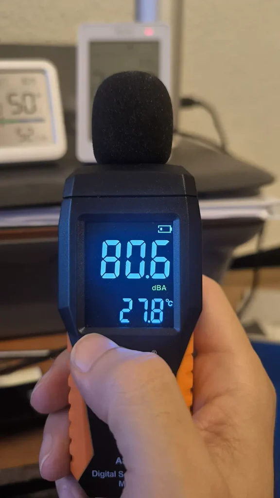 Sonómetro marcando 80,6 dBA mientras suena la alarma del SONOFF AirGuard CO2, que aparece al fondo con la luz de aviso en rojo